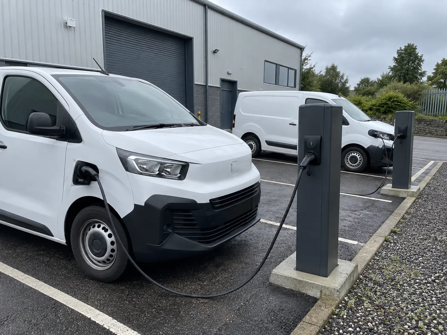 Illustrative electric work vans at workplace charging points (AI-generated)